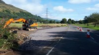 An area of unfinished road forming a junction with a finished road. An excavator is nearby.