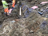 Contractors in PPE standing on earth trenches with red and yellow slabs.