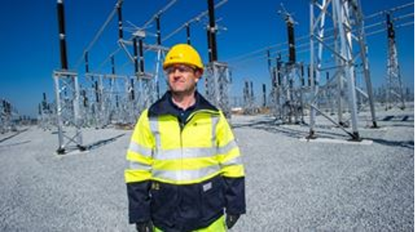Man in PPE stood in front of transmission electrical infrastructure