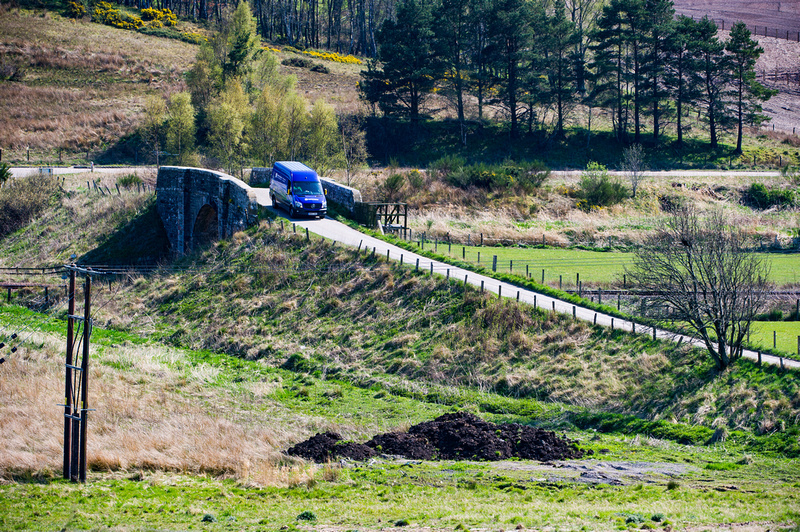 An SSEN Transmission employee in PPE at the wheel of an SSEN Transmission vehicle on a rural road.