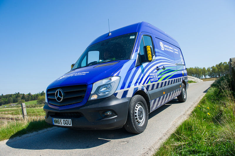 An SSEN Transmission employee in PPE at the wheel of an SSEN Transmission vehicle on a rural road.