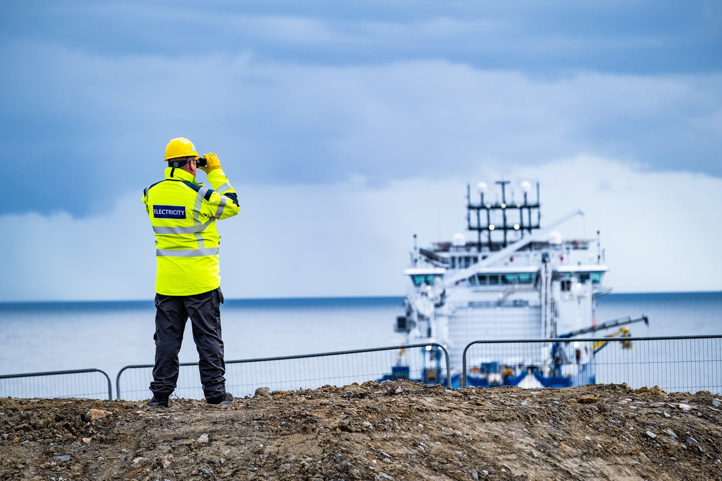 A colleague wearing PPE looking out to a cable laying ship at sea