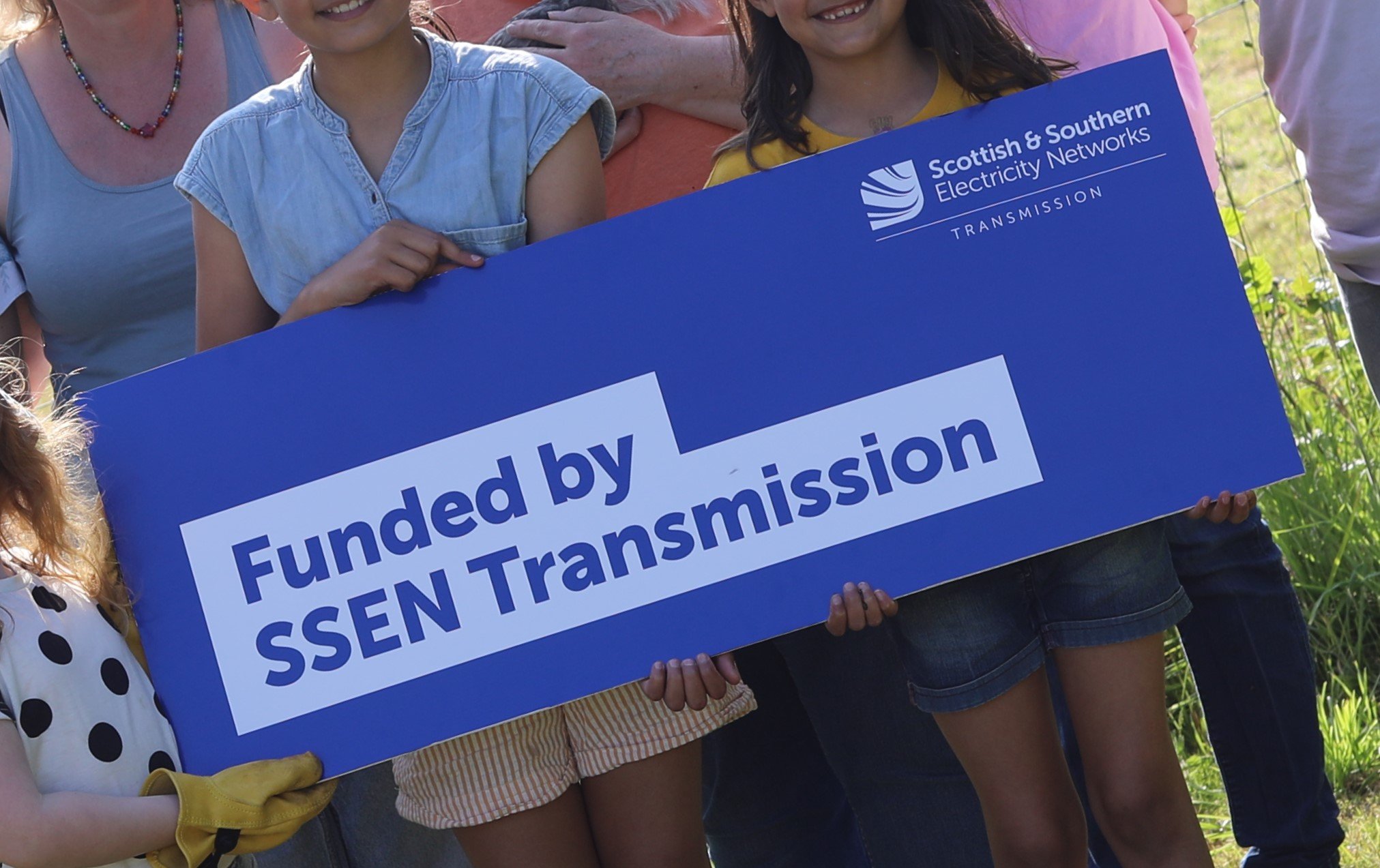 A community group holding a sign which says Funded by SSEN Transmission