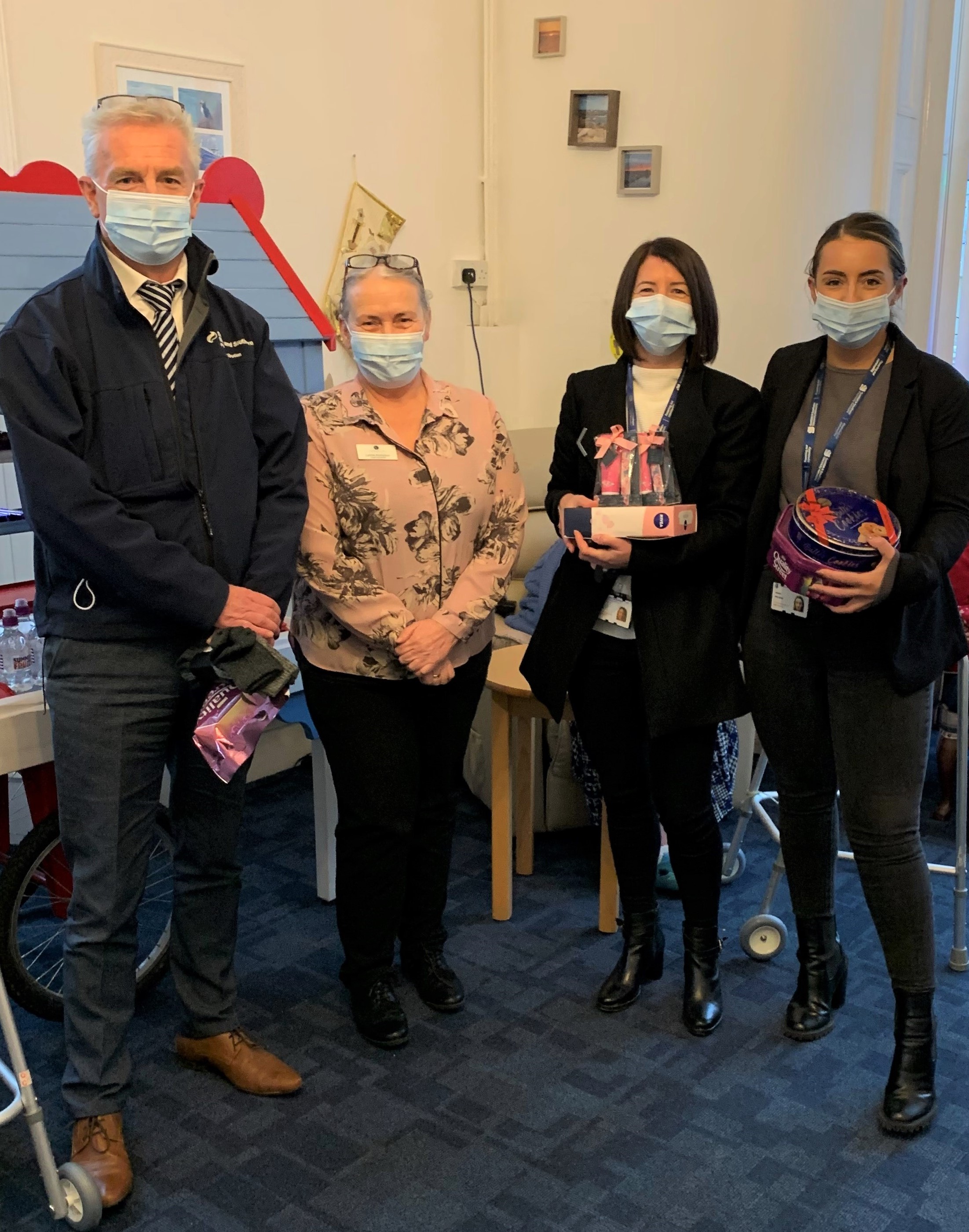 Four people wearing face masks holding donated goods