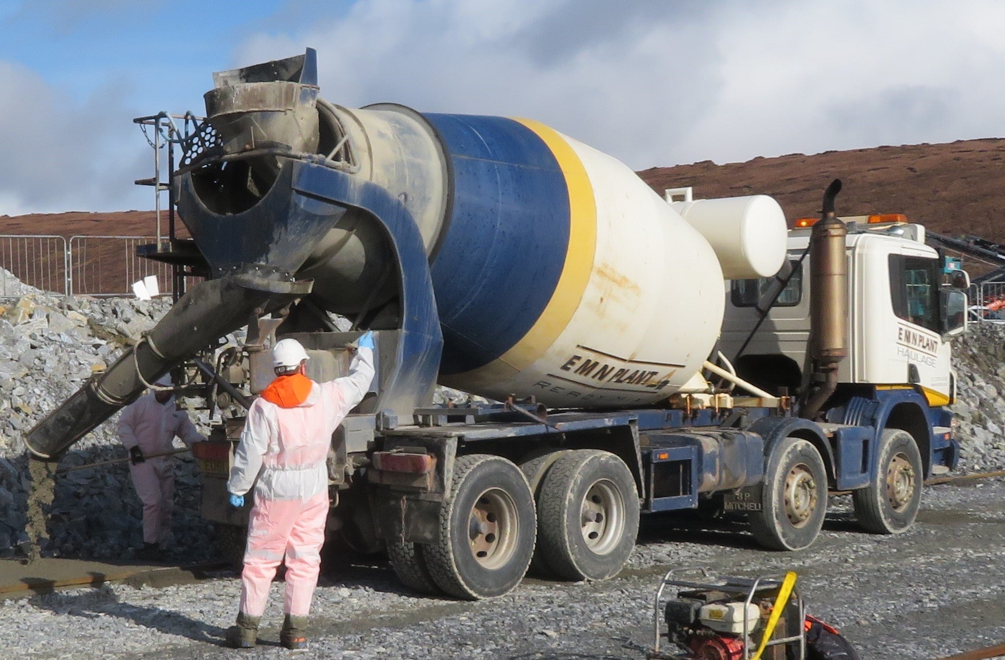 Cement mixer pouring concrete with man in PPE behind
