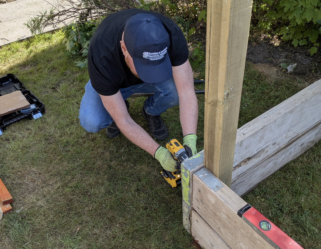 Image of SSEN Transmission employee drilling boards in garden 
