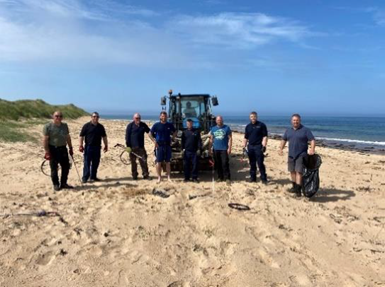 Eight people with litter picking equipment and a tractor standing on a beach