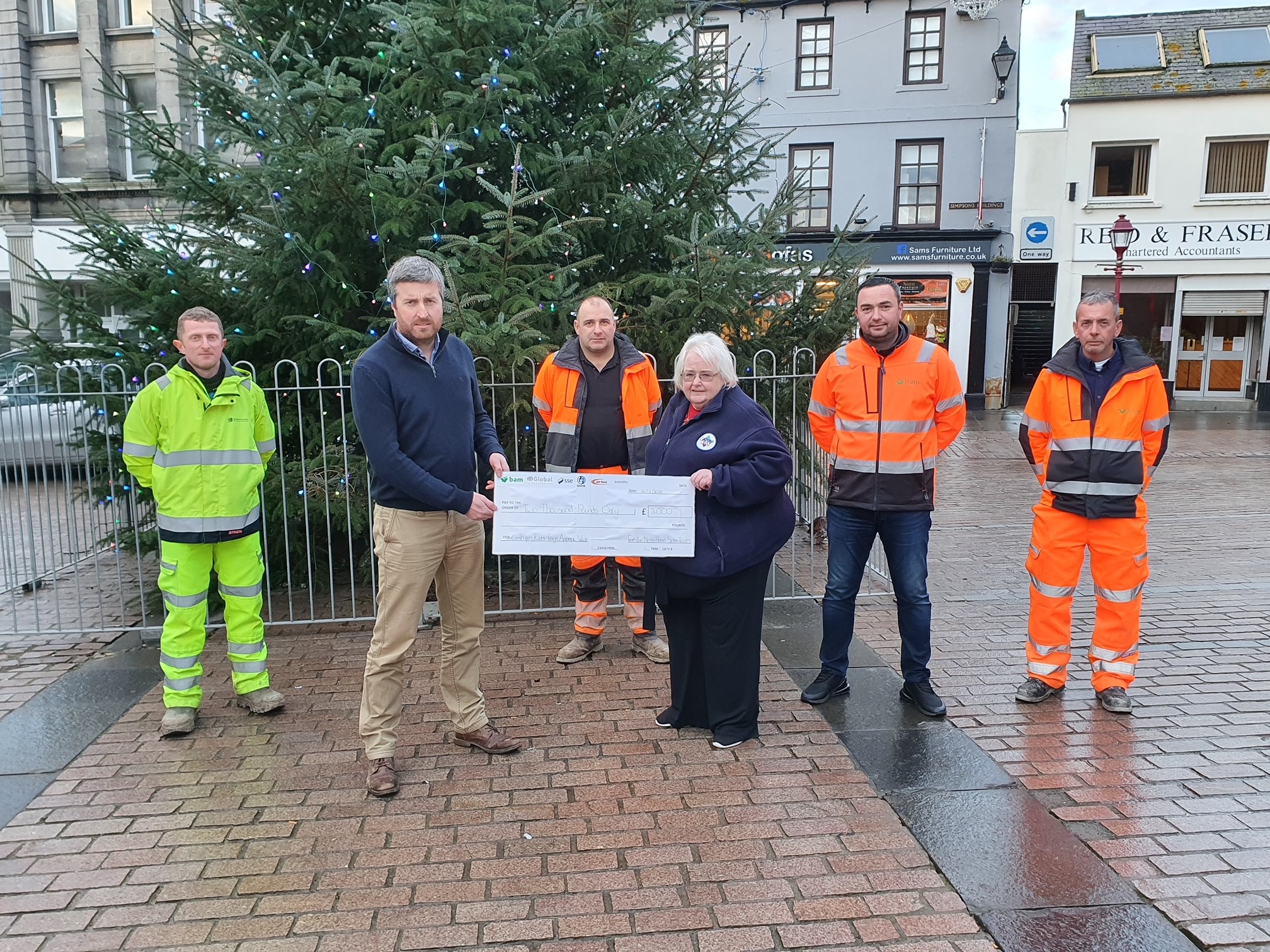 Group of people standing outside in front of Christmas tree with a novelty cheque