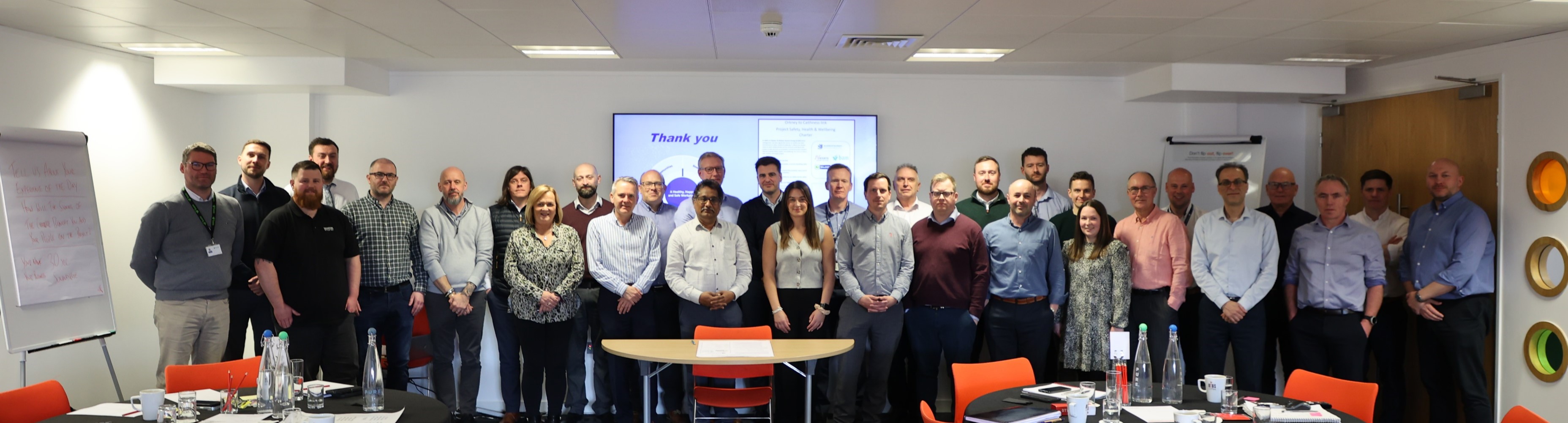 Large group of people standing in an office in front of a presentation
